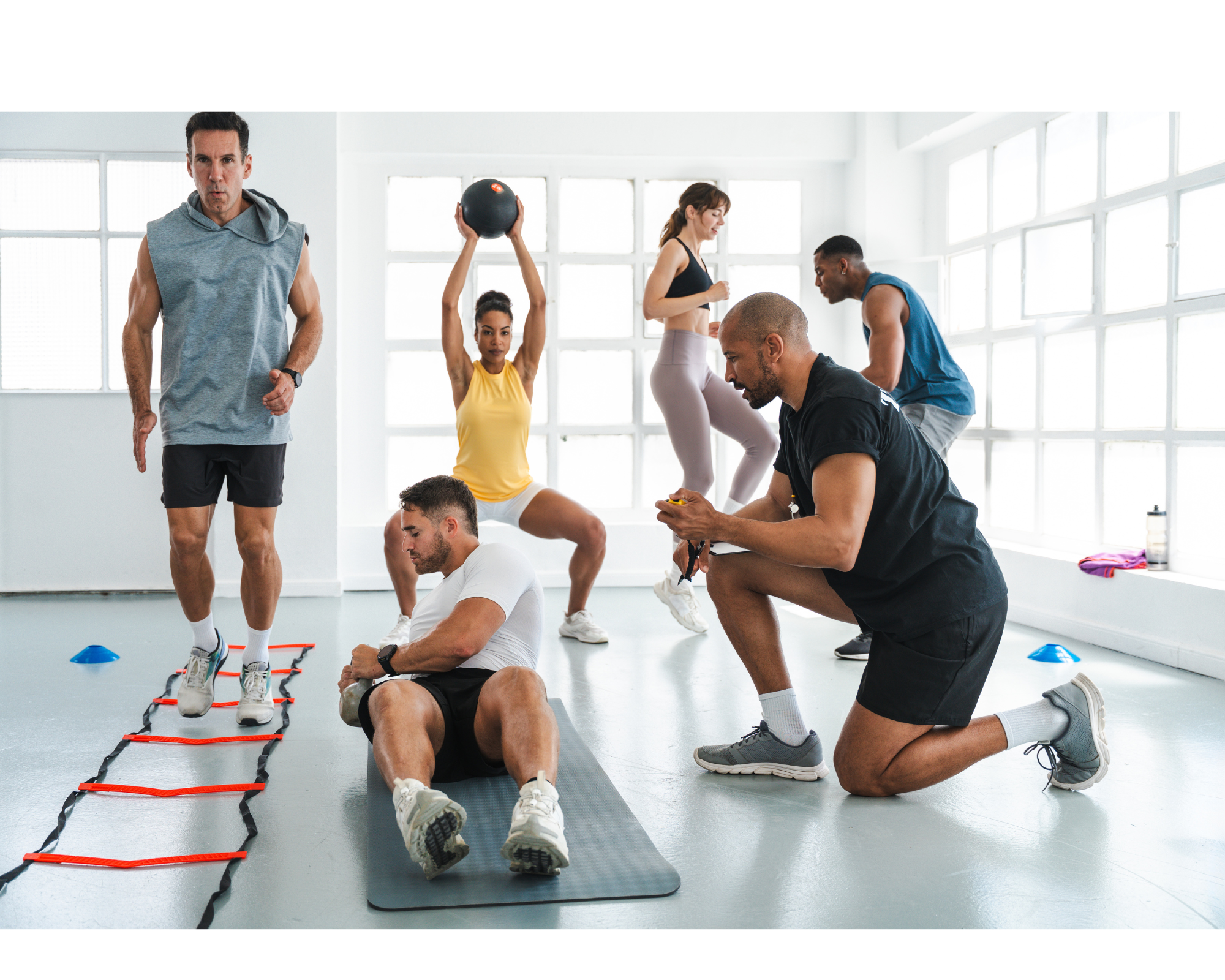 Personal trainer guiding a diverse group of beginners through a circuit workout in a bright fitness studio, demonstrating various exercises including agility drills, medicine ball squats, and core training.