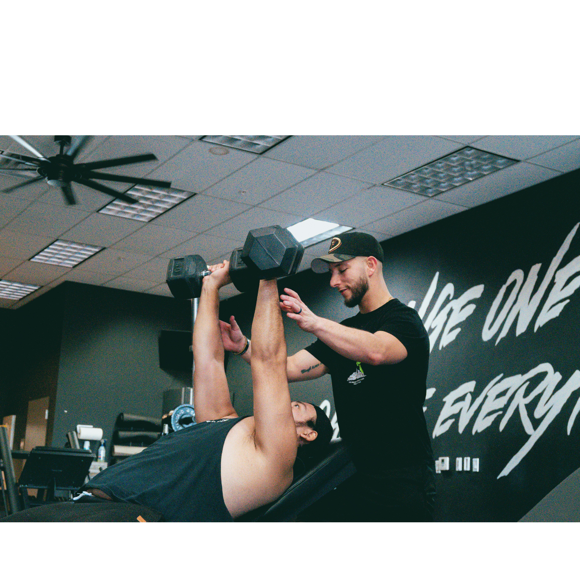 Personal trainer assisting a client with dumbbell chest presses on an incline bench inside a gym, focusing on form and safety during the workout.