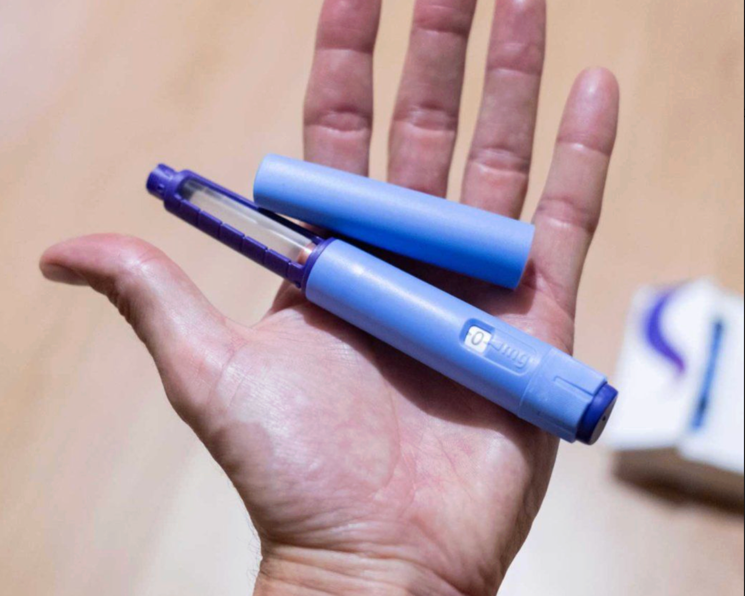 GLP-1 weight loss injection pen held in hand against neutral background